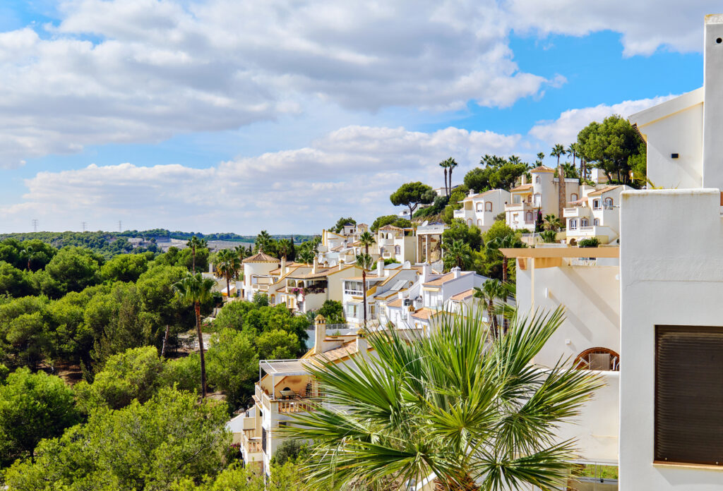 White houses nestled among lush green trees under a partly cloudy sky.